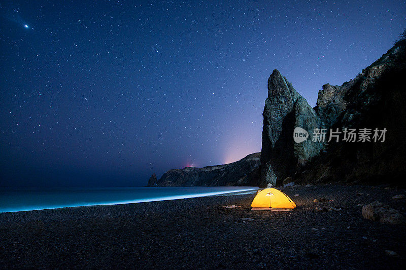 在繁星点点的夜空下，在美丽的海岸上有闪闪发光的帐篷和岩石