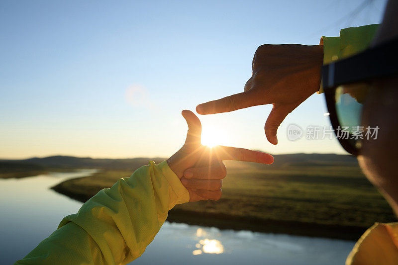 夕阳西下的天空上，人手在做一个框架标志