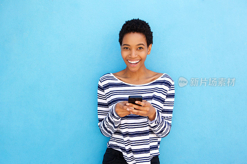 微笑的年轻黑人妇女拿着蓝色背景的手机