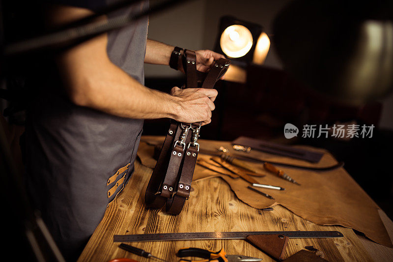 皮带在皮革车间的工作过程。手持摄影师腰带的男子。木制背景上的工具。旧制革厂的皮匠。合上主人的胳膊