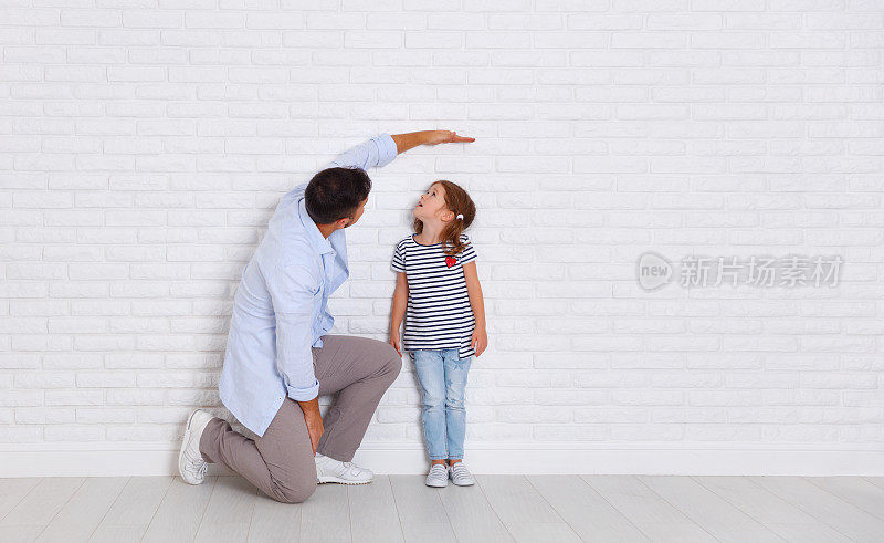 家庭的概念。父亲向女儿测量孩子的成长近空墙