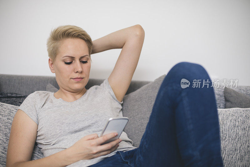 一个年轻漂亮的女人躺在沙发上用智能手机发短信