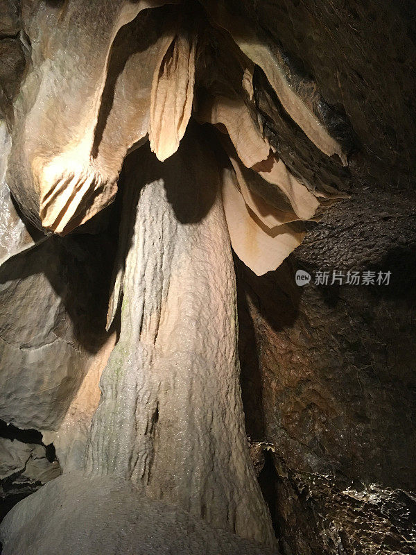 在一个山洞里。由一盏灯照亮的队形。洞穴中巨大的石笋形成。捷克共和国的洞穴探险。洞穴里美丽的钟乳石和石笋。