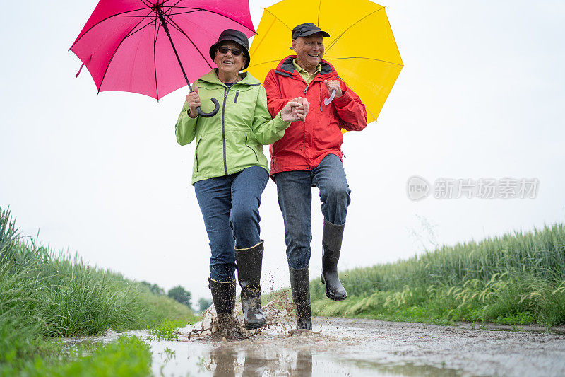 快乐活跃的老年夫妇走过泥泞的雨水坑