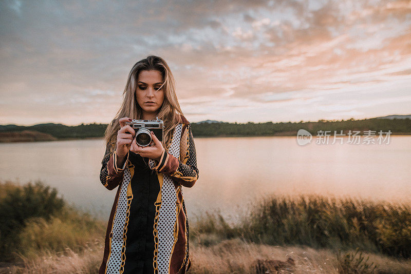 日落时分，一名年轻女子在湖边用老式相机拍照
