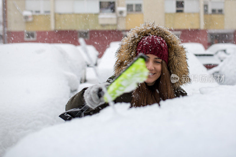 年轻女子在清理车上的积雪