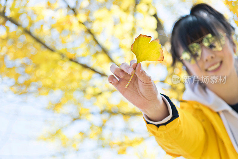 拿着一片黄色银杏叶的女人