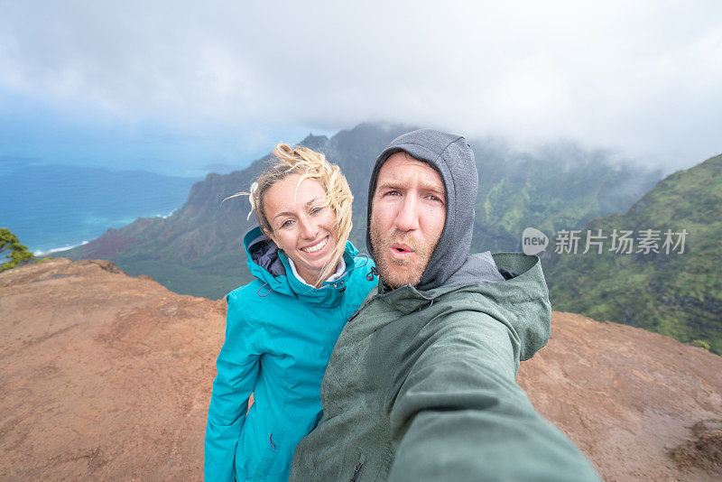 欢快的年轻夫妇在雨中徒步旅行时拍自拍照。摄于夏威夷考艾岛