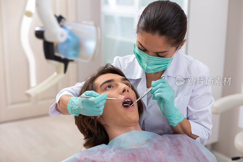 女牙医在看一位男性病人的口腔