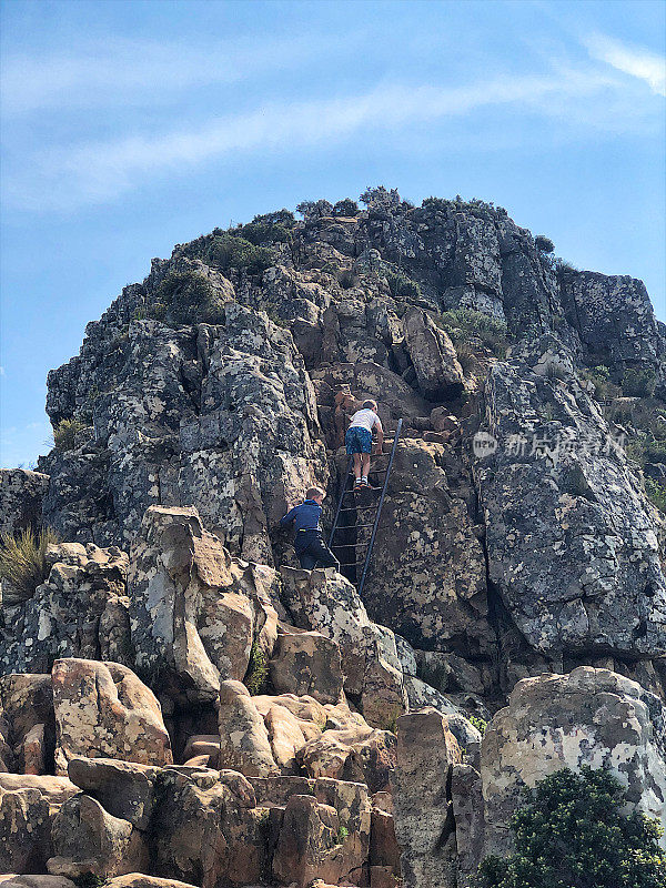 两个男孩正在爬铁梯，沿着岩壁爬向山顶