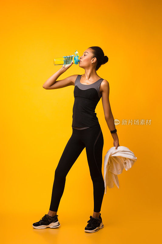 运动的非洲裔美国女士在工作室锻炼期间喝水