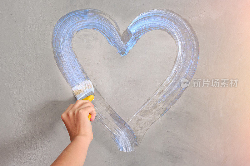 一个女人的手用白漆在墙上画一颗心，复制空间。女孩在混凝土墙上画了一幅浪漫的画。
