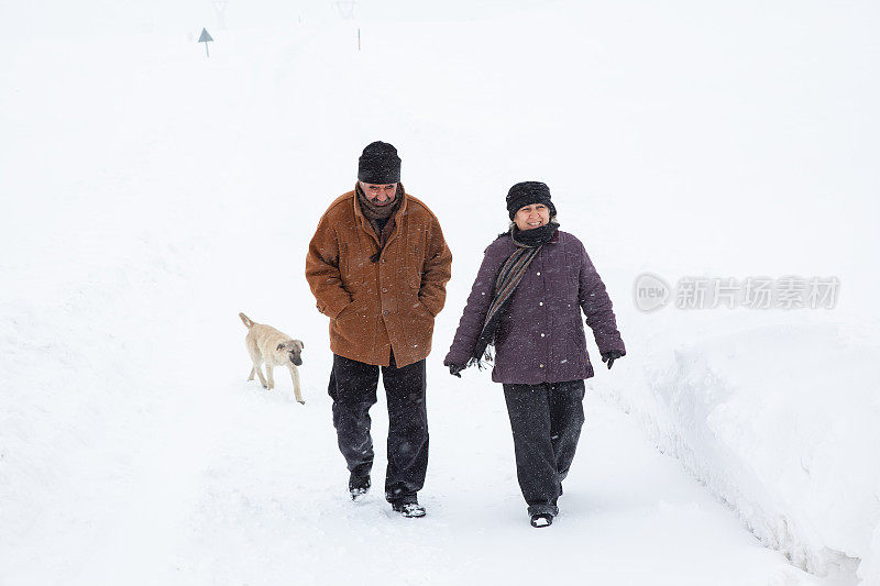 一对老年夫妇在下雪的乡村路上穿着暖和的衣服