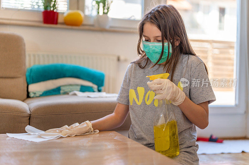 年轻女孩戴着防护面罩和防护手套在家清洁桌子