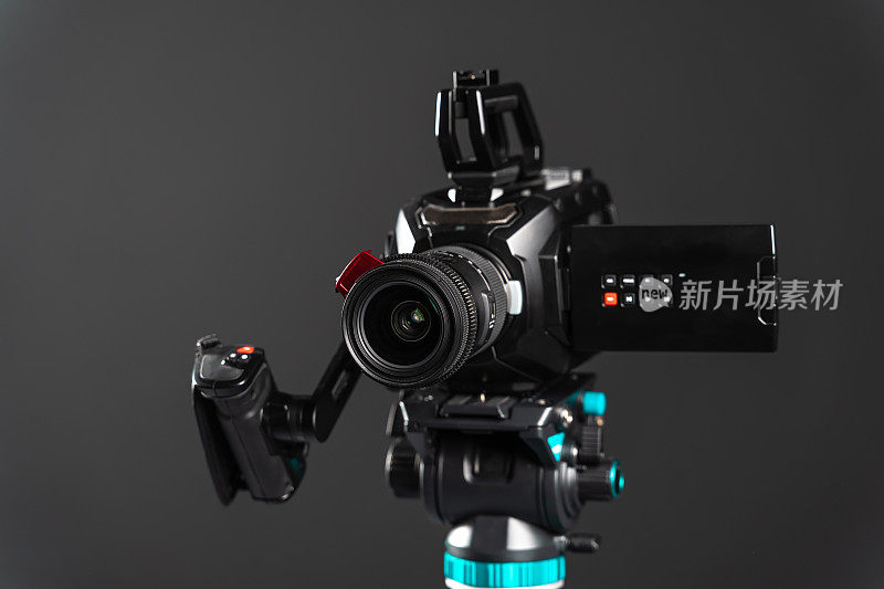 专业的视频电影摄像机在一个摄像机三脚架上，黑色的工作室背景