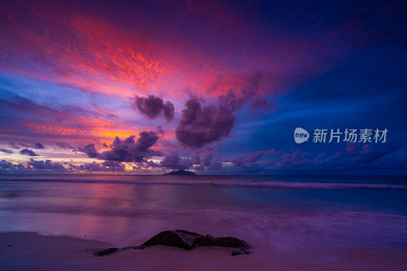 日落后热带岛屿、海滩和海洋上的绚丽多云的天空