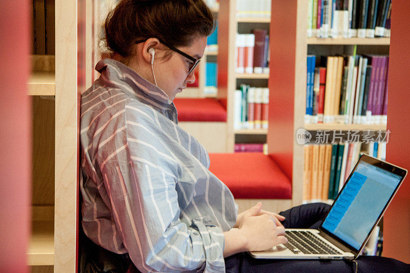 女学生在图书馆使用手提电脑和耳机