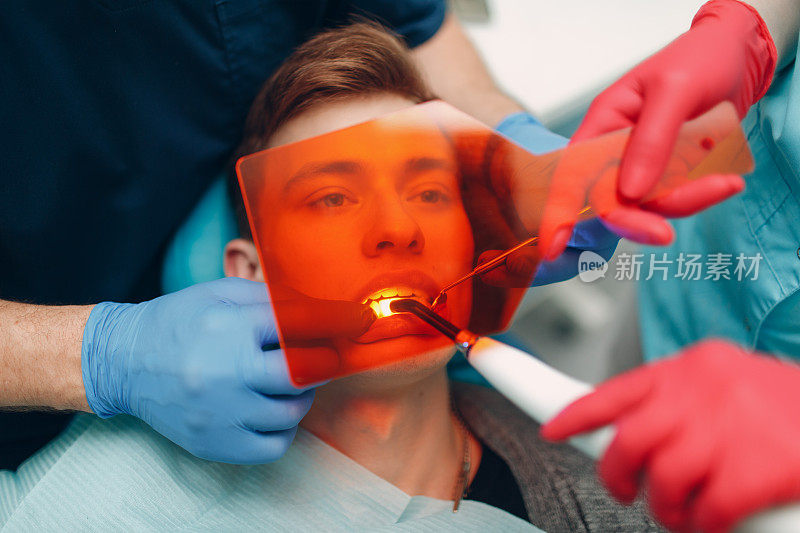 牙医。牙医和病人。光固化密封。紫外线牙科灯和橙色保护玻璃。补牙材料。