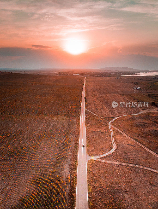 汽车在日落时行驶在笔直的乡村道路的鸟瞰图