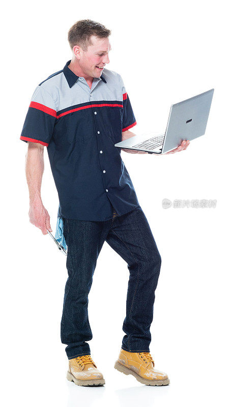 白人体力劳动者穿着制服站在白色背景前，手持扳手，使用笔记本电脑