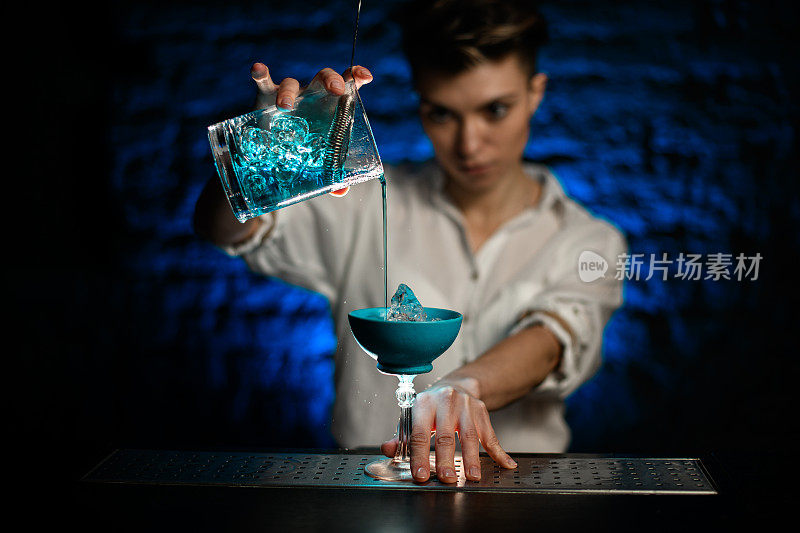 女调酒师将蓝色鸡尾酒从混合杯倒入玻璃杯