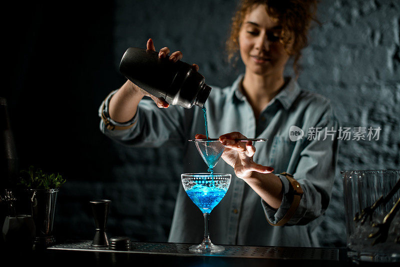 酒吧里的女孩把亮蓝色的饮料从摇酒器倒进杯子里