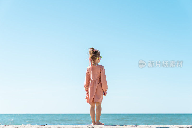 一个五岁的小女孩背对着大海站着。