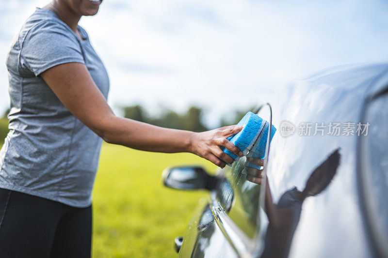 快乐的混血儿女人用海绵清洁汽车