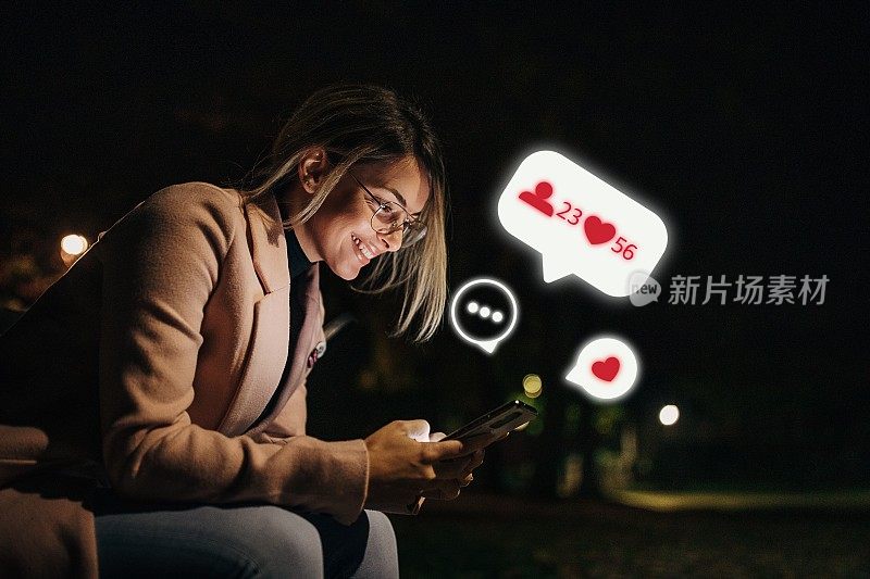 晚上在公园里坐着用手机玩社交网络的美女