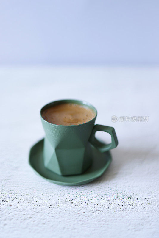 在浅灰色的混凝土地板上，绿色的陶瓷杯子里装着土耳其咖啡，正视图，杯子的形状像折纸