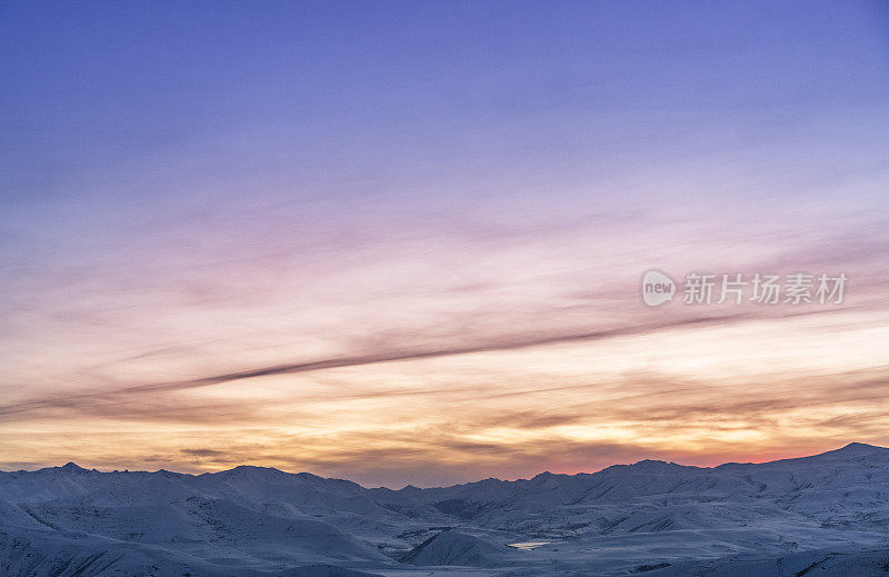 美丽的冬天的风景。日落时，山顶上覆盖着积雪。戏剧性的天空。