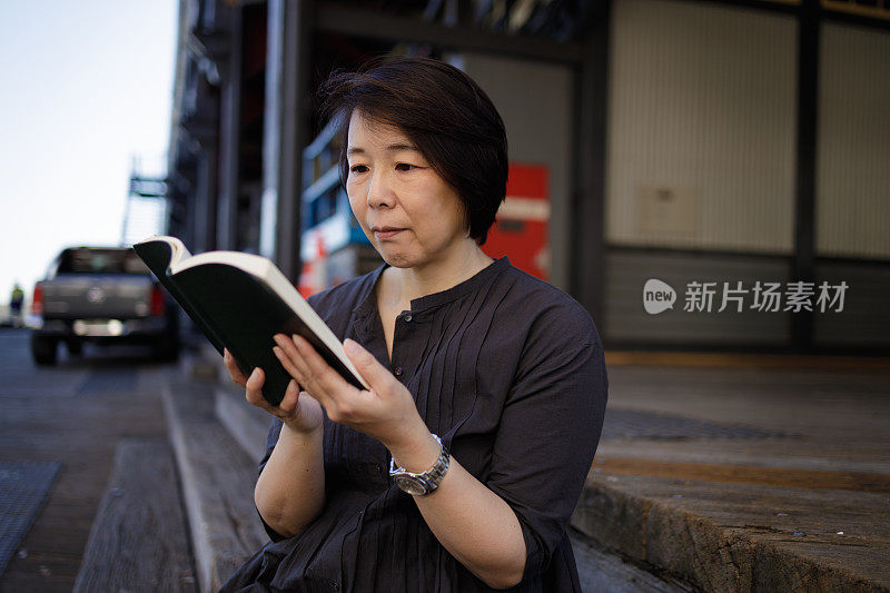 亚洲妇女在户外木制台阶上阅读