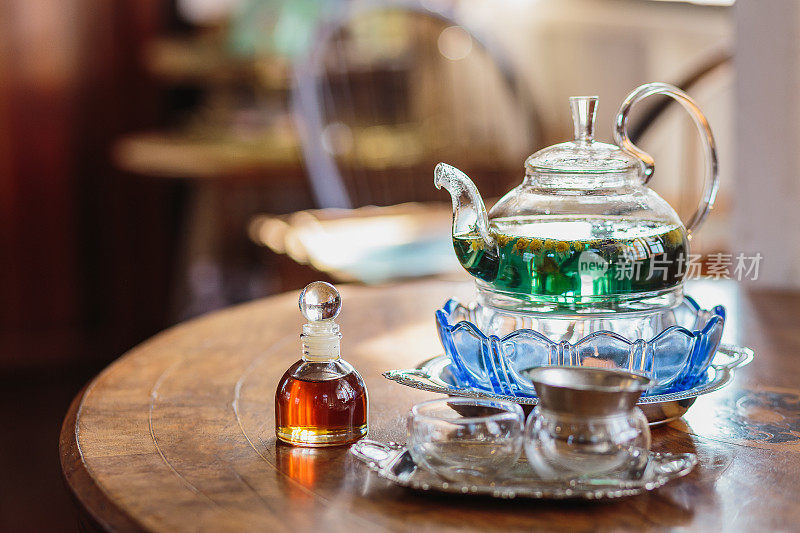 家里的木桌上放着玻璃茶壶、茶杯和糖浆瓶