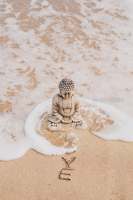 美丽的佛像，脸上有一滴泪珠坐在海滩上，在海浪包围着他和写在沙滩上的爱的字