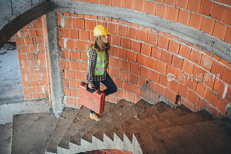 年轻的女建筑工在建筑工地搬运工具箱