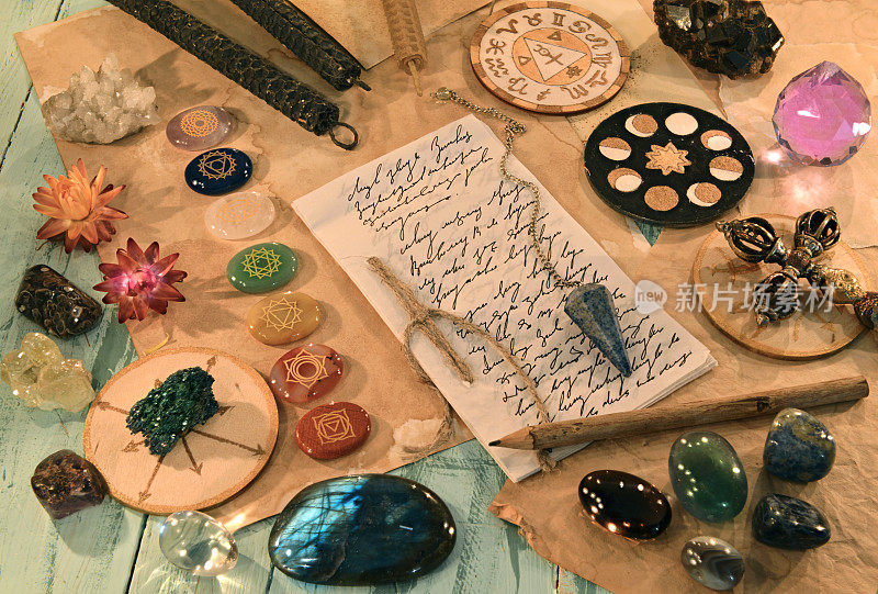 水晶石与脉轮，蜡烛，仪式物品和纸上的字母和文字在桌子上。