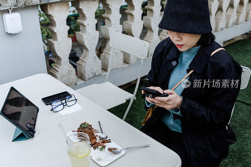 一名亚洲年轻女子在户外咖啡馆的数字桌子上工作时使用智能手机