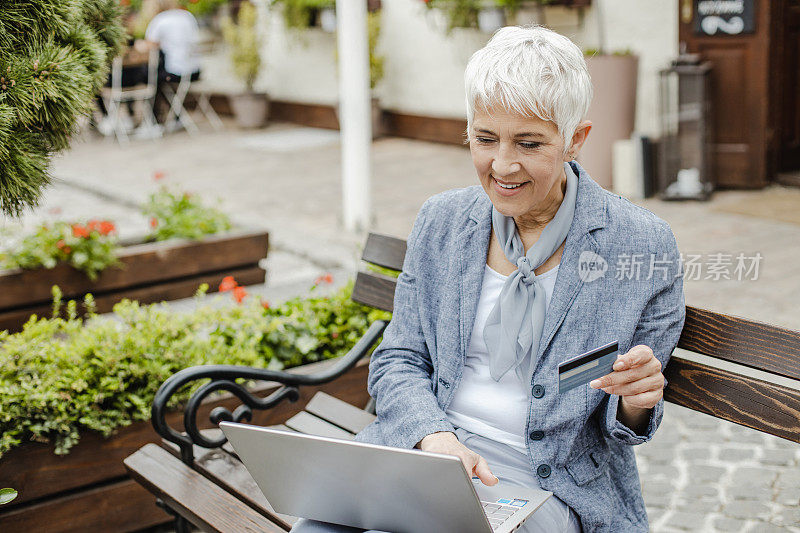 一个成熟的女人在街上用笔记本电脑在网上购物