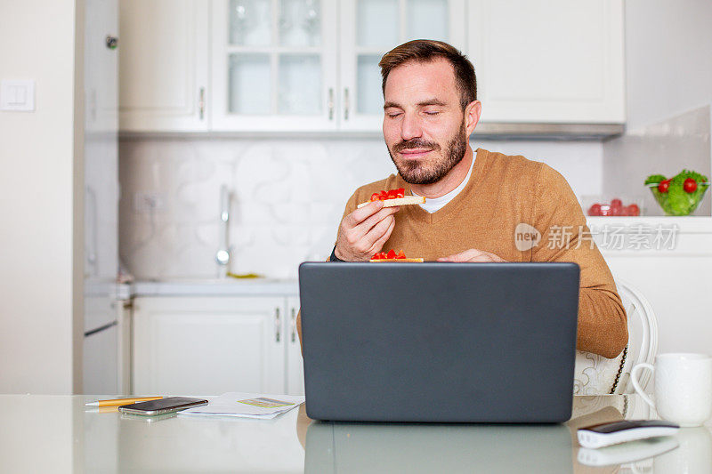 一位年轻人正在享受妻子给他做的健康零食。自由职业者正坐在桌子前，笔记本电脑摆在他面前，他正在吃饭。