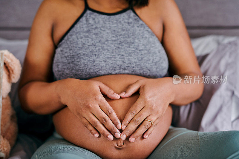 这张照片拍摄的是一个不知名的女人在家里用手在怀孕的肚子上画一个心形