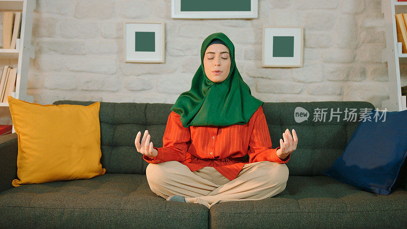 穆斯林妇女戴着头巾在家练习瑜伽。冥想。绑定角度姿势。