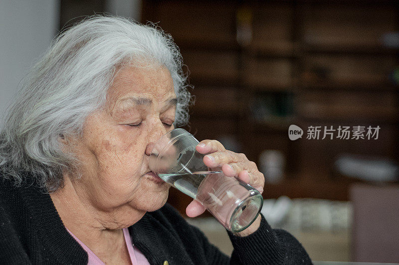一名老人在家喝水的画像