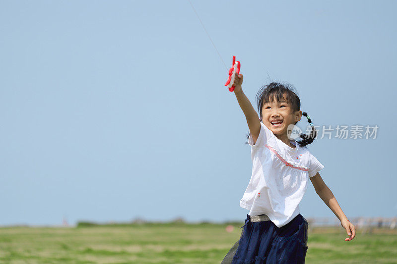 亚洲女孩在草地上玩和放风筝。