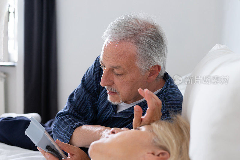 一对老夫妇早上躺在床上，妻子感觉不舒服，丈夫在测量她的血压