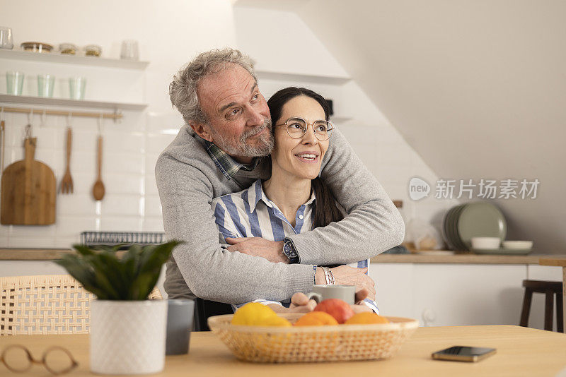 成熟的男人拥抱他的妻子，在厨房里享受