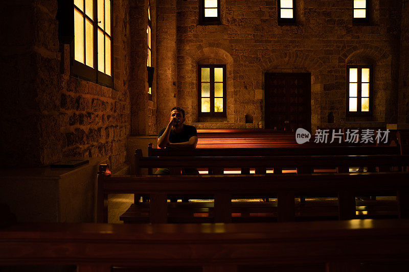 一个年轻人坐在教堂里的长凳上祈祷