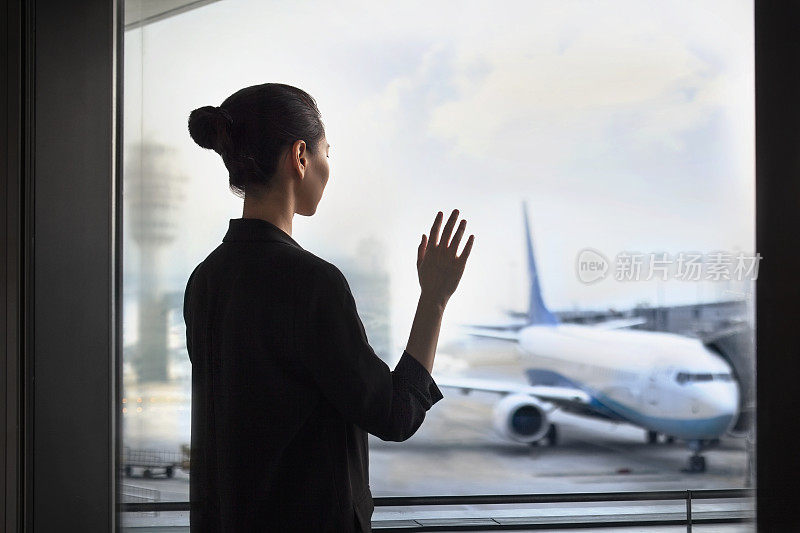 年轻的中国女子站在机场候机楼出发区向飞机挥手