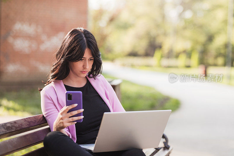 女人在公园里用笔记本电脑和手机，还皱着眉头