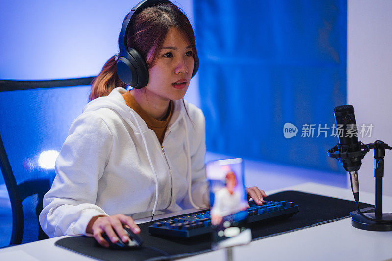 年轻的亚洲女性在家里的霓虹灯客厅里玩在线电脑游戏和直播。