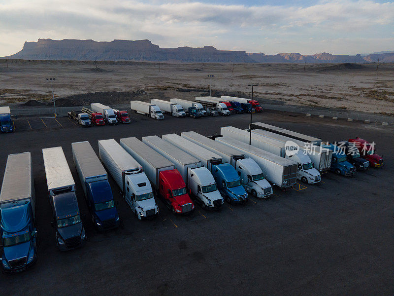 在犹他州东部沙漠地区70号州际公路上的一个大型停车场，半挂卡车排队等待晚上在一个戏剧性的云景日落天空下